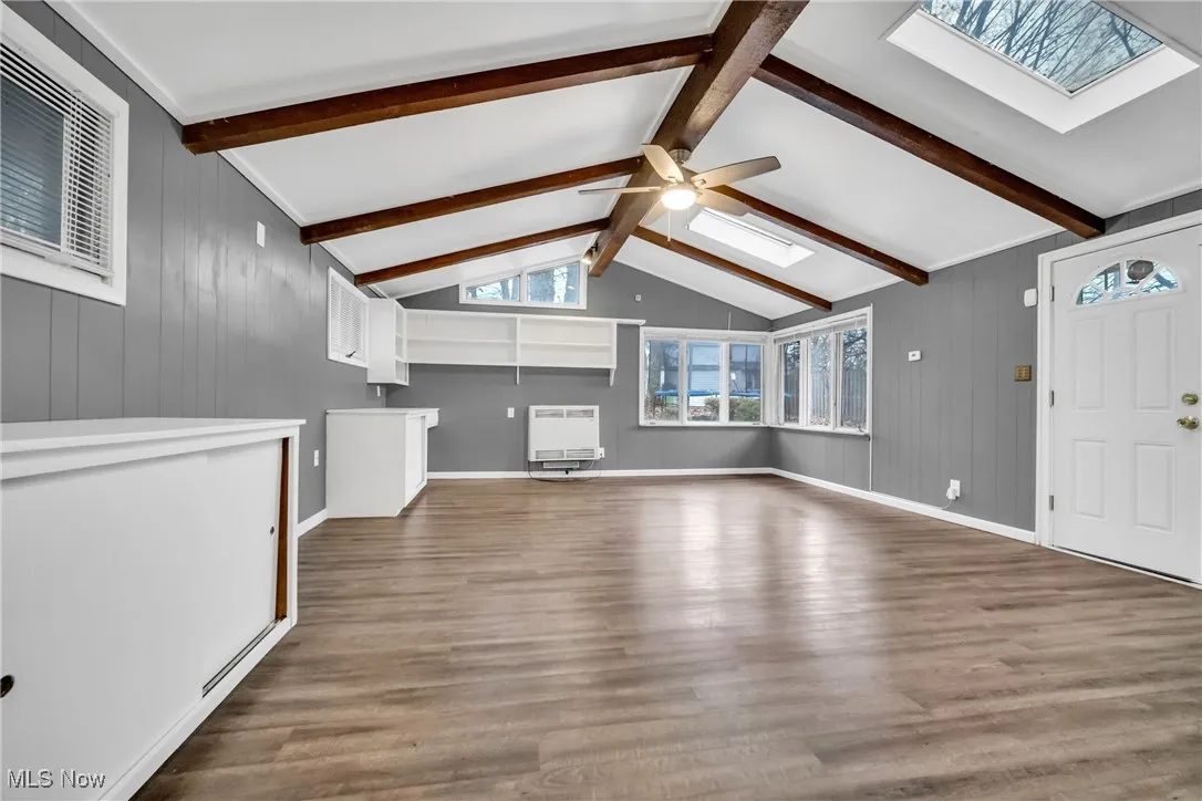 Unfurnished living room with visible vents, heating unit, wood finished floors, and lofted ceiling with skylight