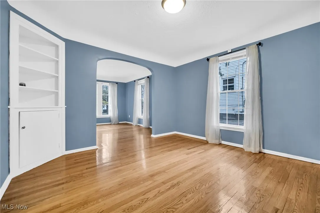 Unfurnished room with baseboards, wood finished floors, arched walkways, and built in features