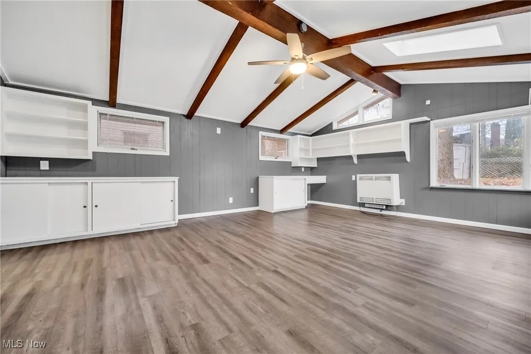 Unfurnished living room featuring vaulted ceiling with skylight, wood finished floors, ceiling fan, and heating unit