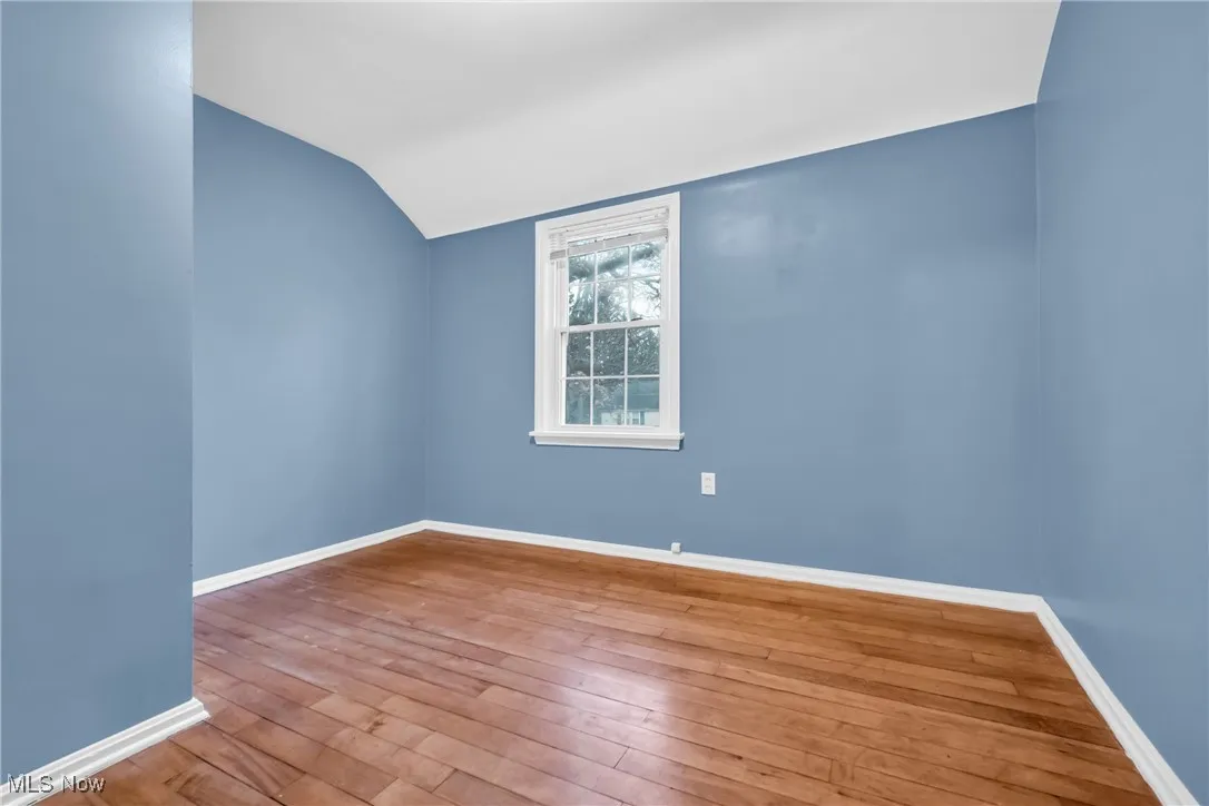 Unfurnished room with lofted ceiling, hardwood / wood-style floors, and baseboards
