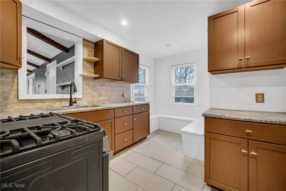 Kitchen featuring open shelves, gas stove, decorative backsplash, and a sink
