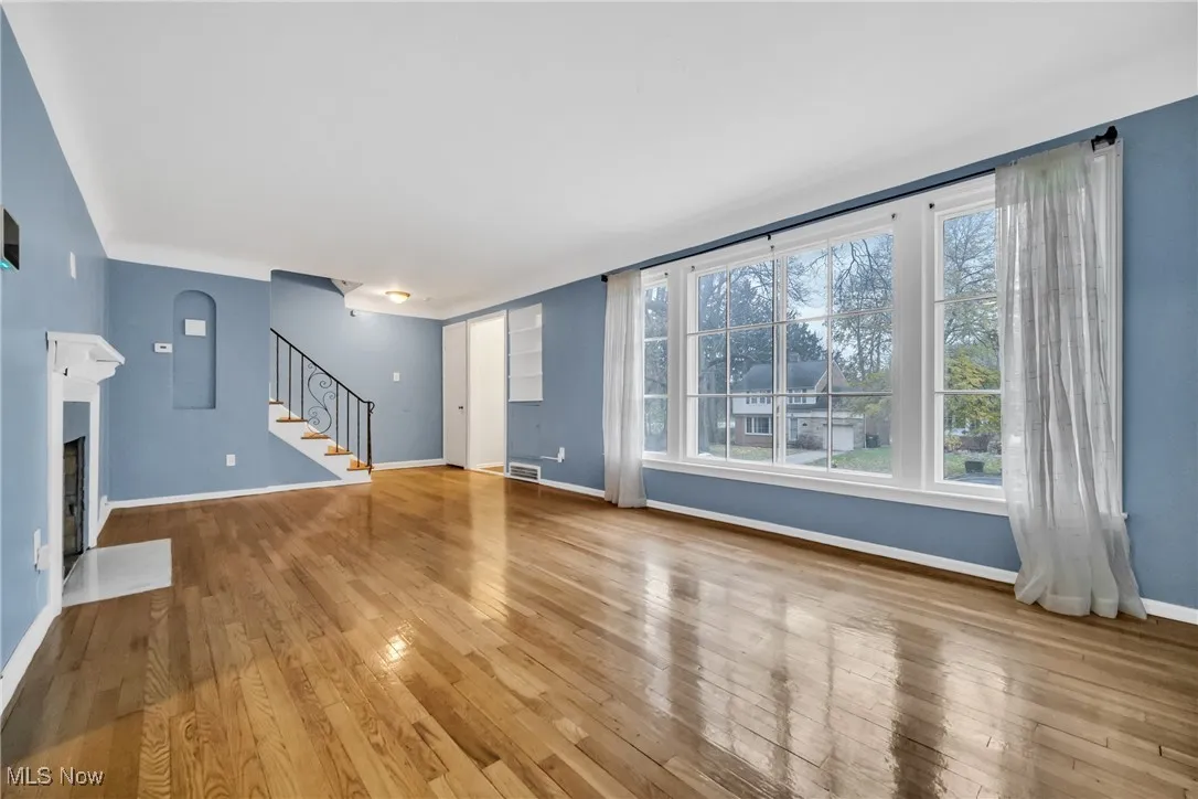 Unfurnished living room with a fireplace with flush hearth, stairway, hardwood / wood-style floors, and plenty of natural light