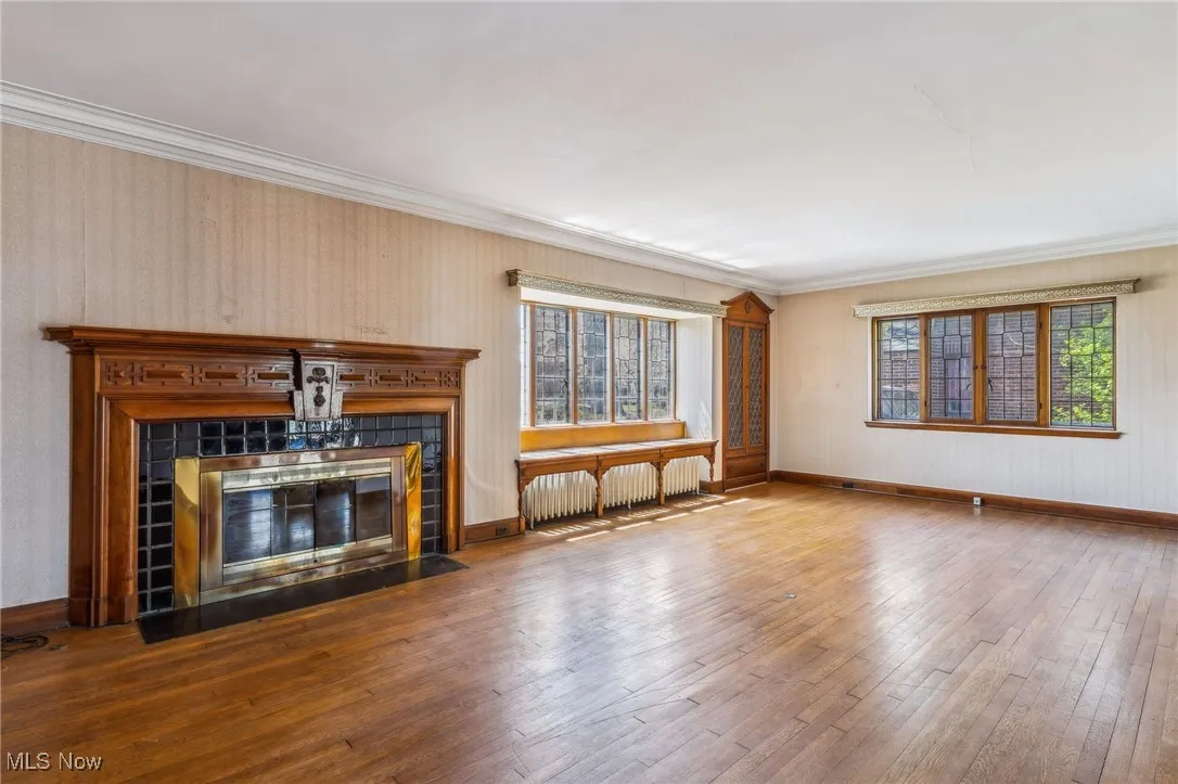 Unfurnished living room featuring radiator heating unit, a tile fireplace, ornamental molding, and wood-type flooring