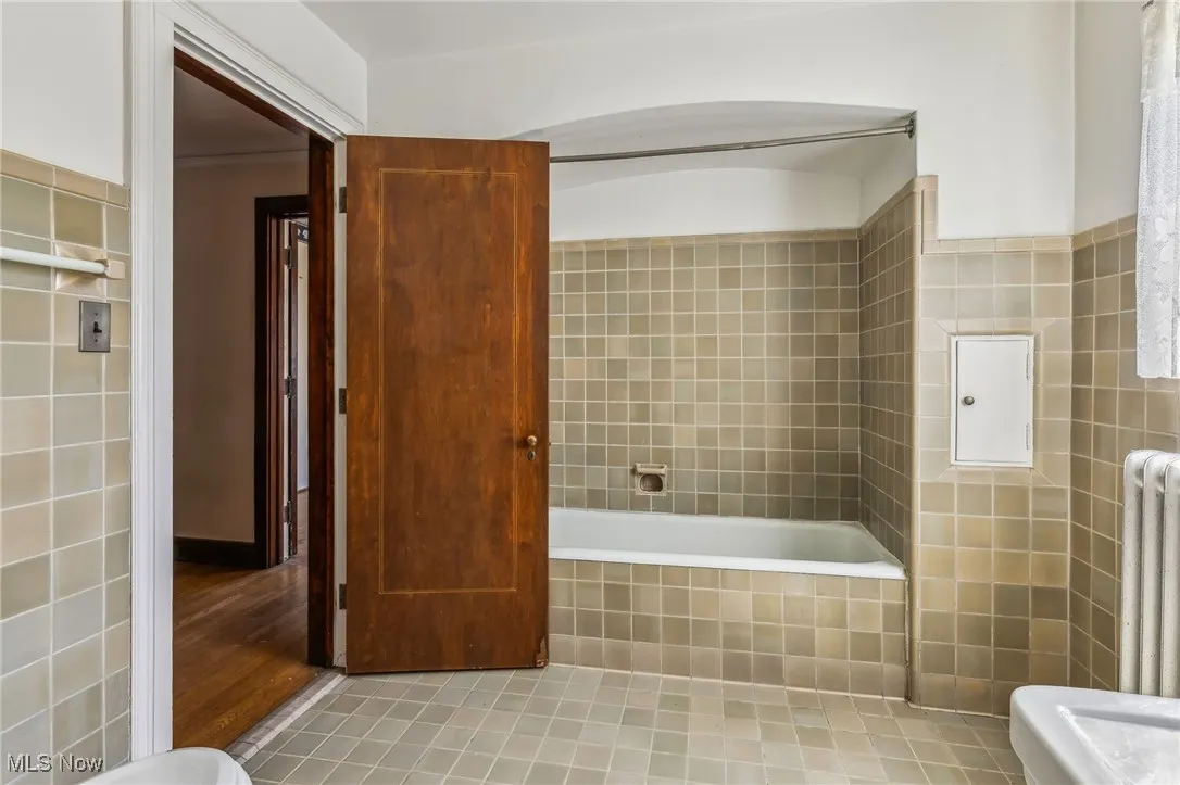 Bathroom with walk in shower, radiator heating unit, tiled bath, and tile walls