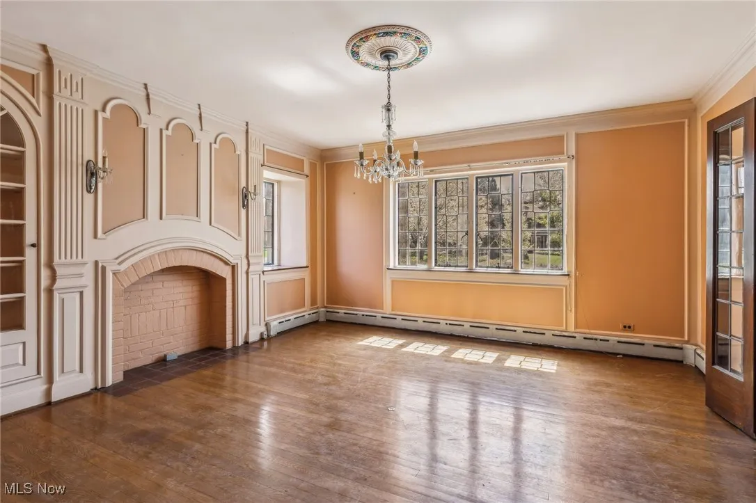 Unfurnished living room featuring a baseboard heating unit, wood-type flooring, crown molding, and a notable chandelier