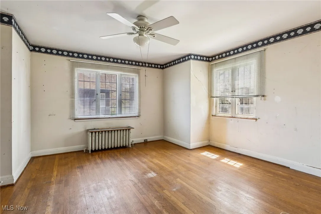 Empty room featuring wood-type flooring, ceiling fan, plenty of natural light, and radiator