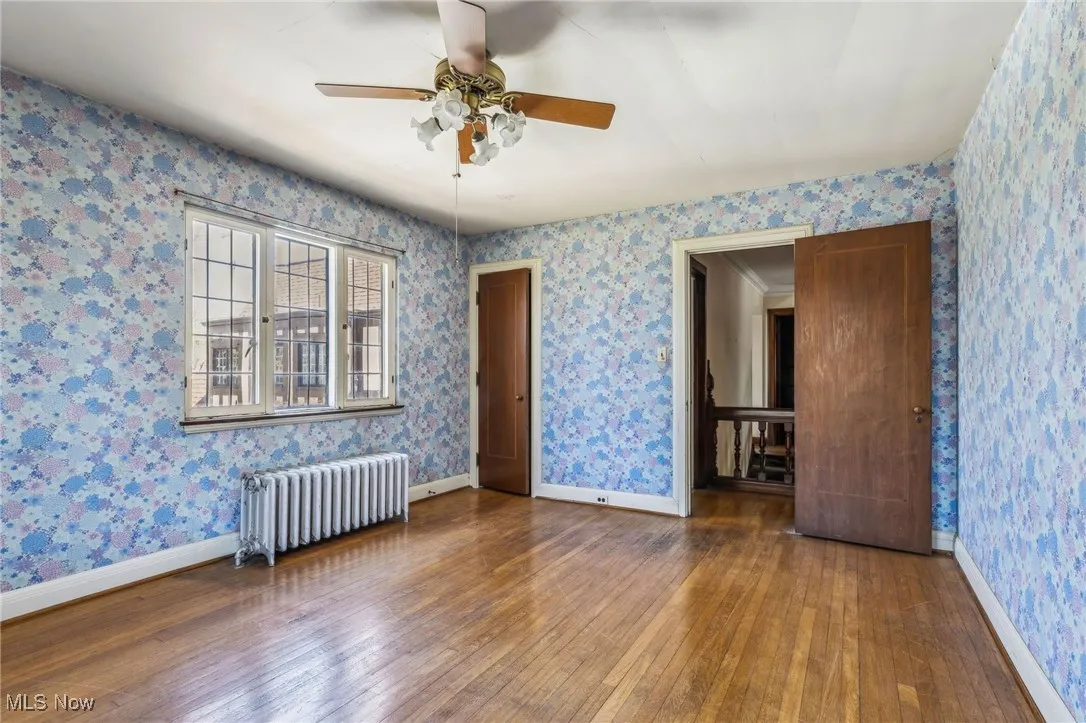 Unfurnished room with radiator, baseboards, a ceiling fan, and wood-type flooring