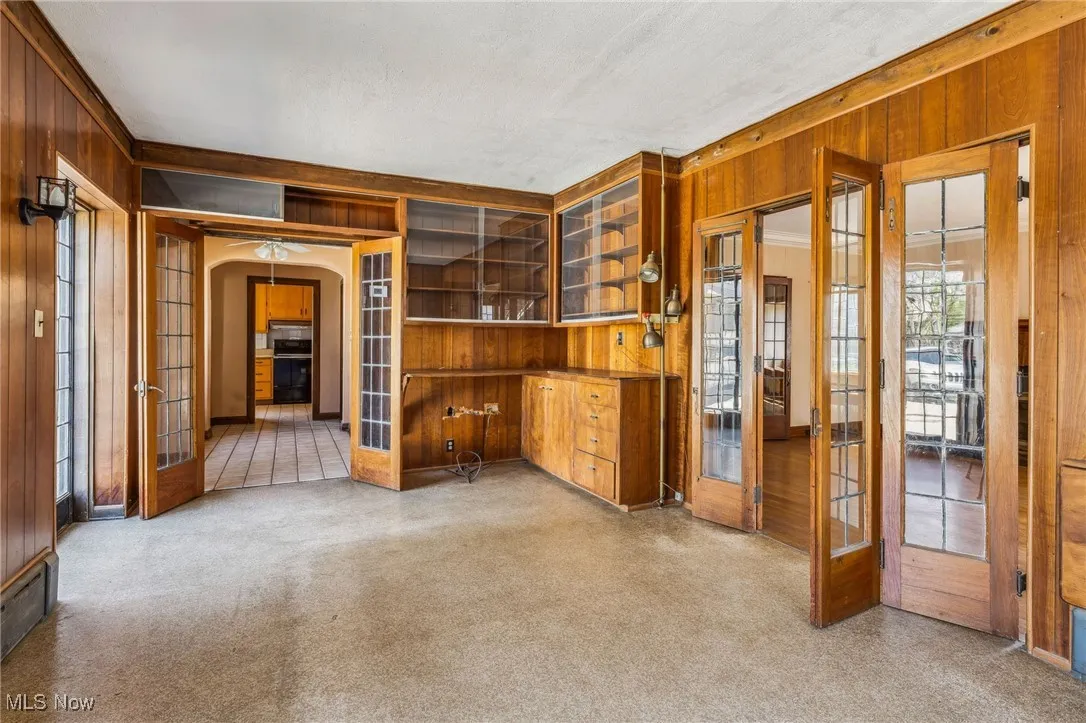 Unfurnished living room featuring arched walkways, visible vents, french doors, and wooden walls