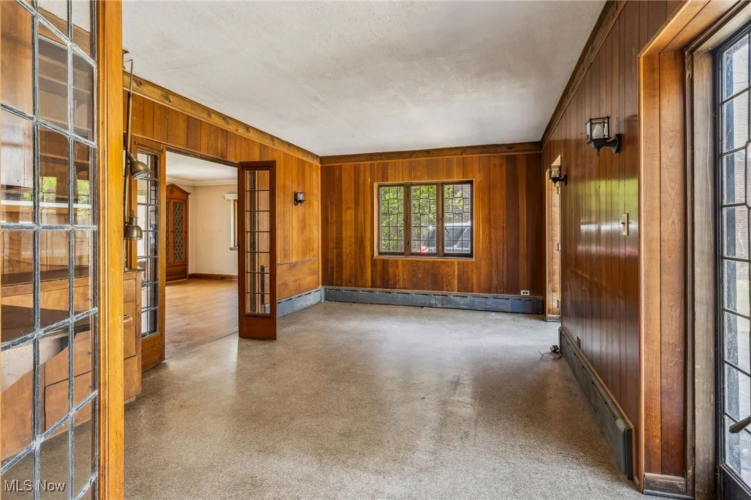 Spare room with a baseboard heating unit, wooden walls, baseboards, and french doors