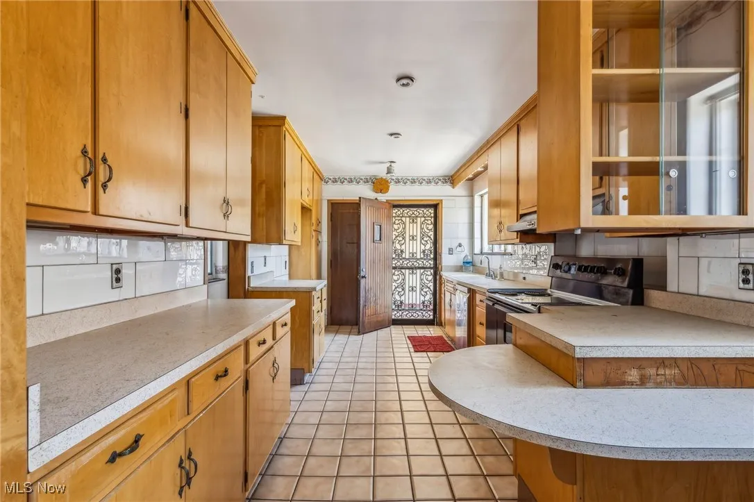 Kitchen with stainless steel appliances, under cabinet range hood, light countertops, light tile patterned flooring, and decorative backsplash