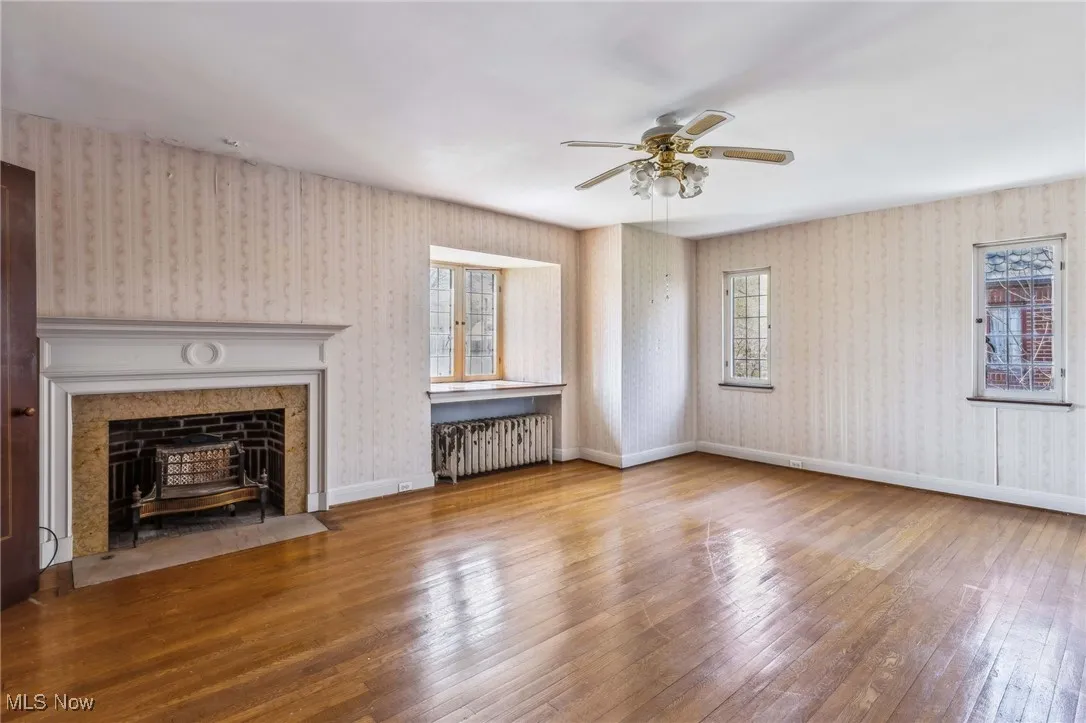 Unfurnished living room with radiator, wallpapered walls, wood-type flooring, and ceiling fan