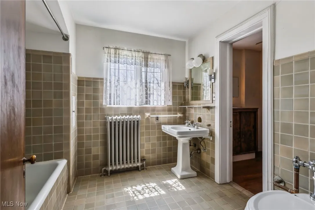 Bathroom featuring radiator heating unit, tile patterned floors, a relaxing tiled tub, a sink, and tile walls