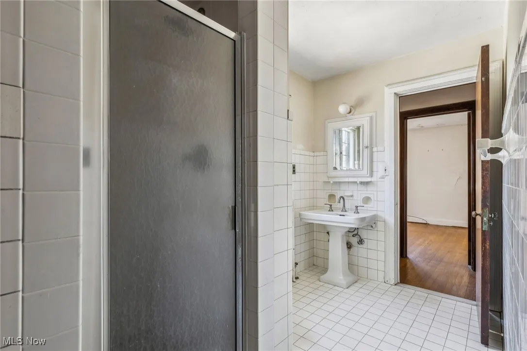 Full bathroom with tile walls, tile patterned flooring, a stall shower, and a wainscoted wall
