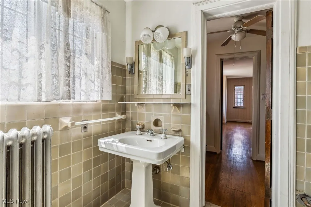 Bathroom featuring radiator, a ceiling fan, wood finished floors, and tile walls
