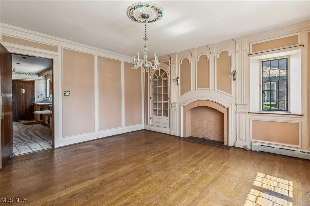 Unfurnished living room with a baseboard heating unit, wood finished floors, a chandelier, and a fireplace with flush hearth
