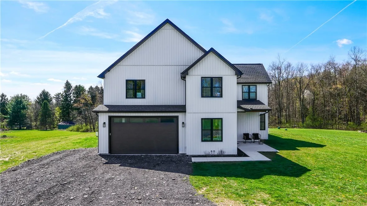View of front of house featuring an attached garage, gravel driveway, a front lawn, and roof with shingles