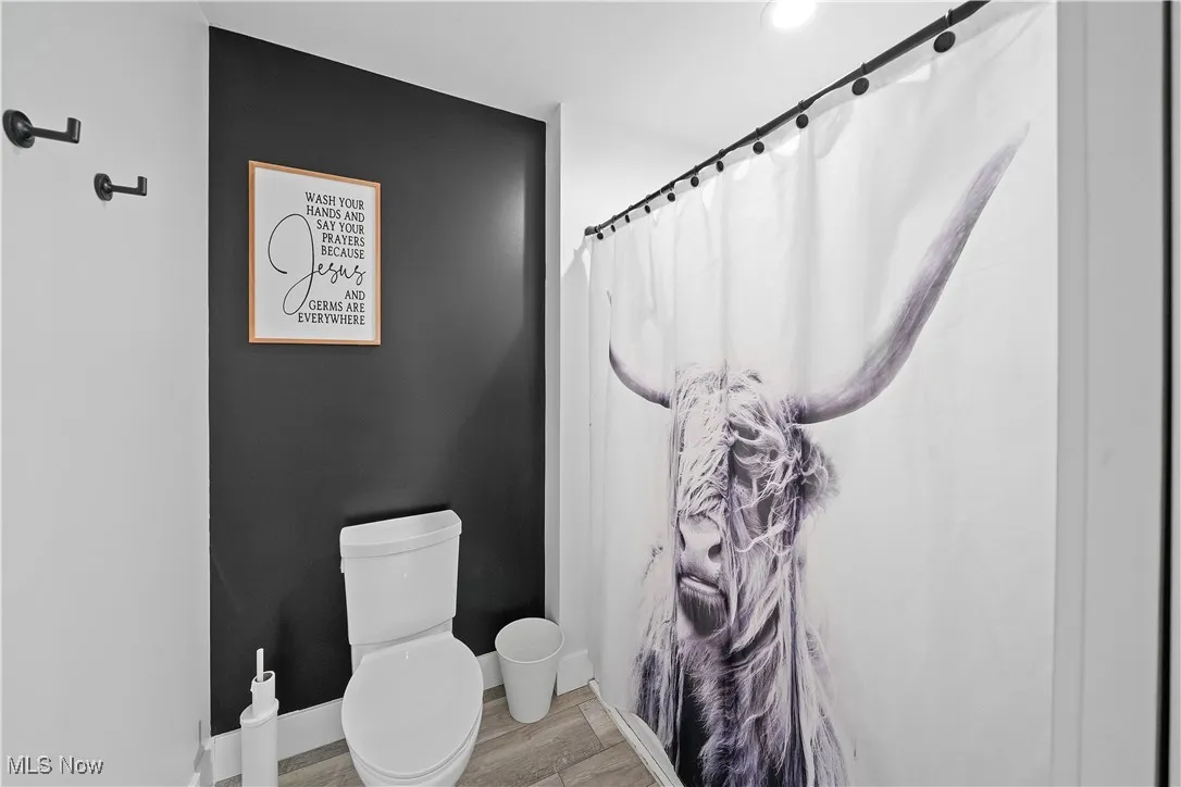 Full bath with baseboards, toilet, wood finished floors, and curtained shower