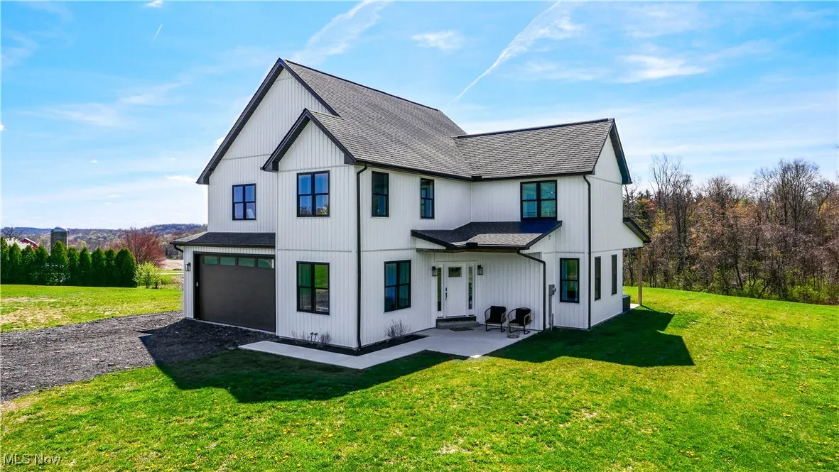 Back of property with a garage, driveway, a shingled roof, and a lawn