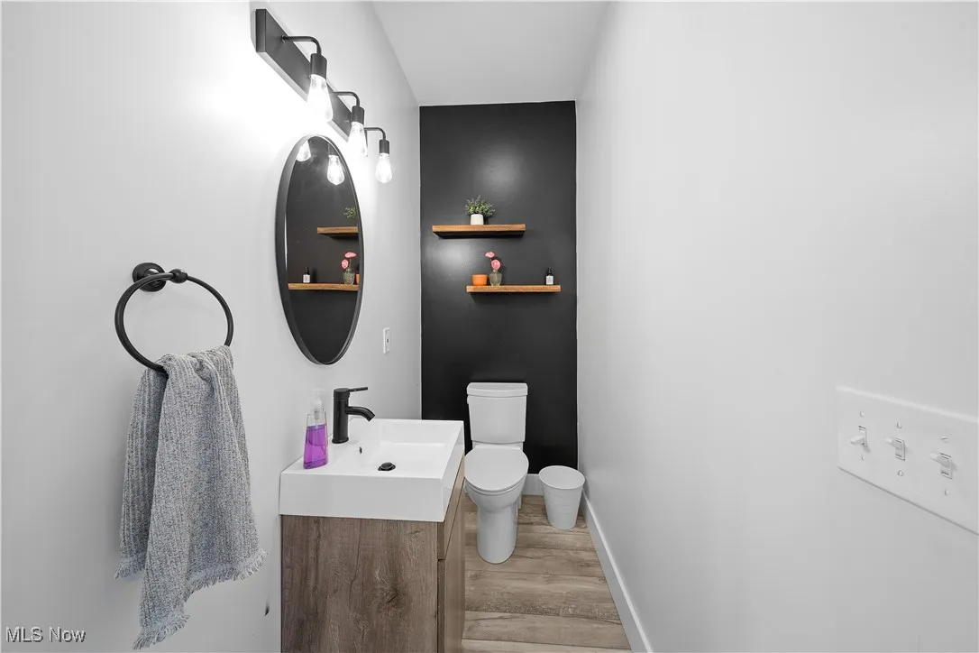 Half bath featuring baseboards, wood finished floors, toilet, and vanity