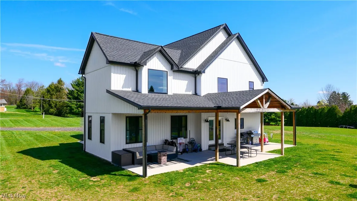 Back of house featuring outdoor lounge area, a patio area, a lawn, and a shingled roof