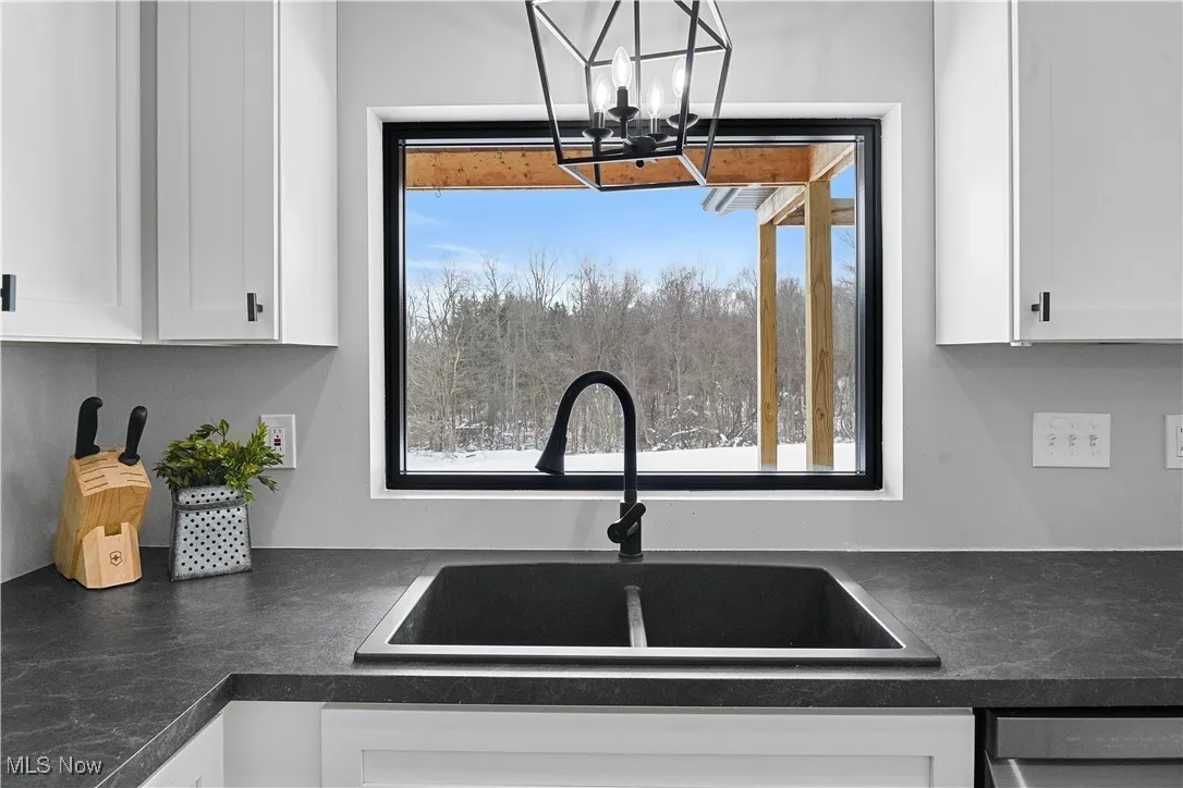 Kitchen featuring dark countertops, a sink, white cabinetry, and an inviting chandelier