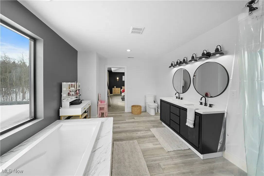 Full bathroom with recessed lighting, double vanity, visible vents, toilet, and wood finished floors
