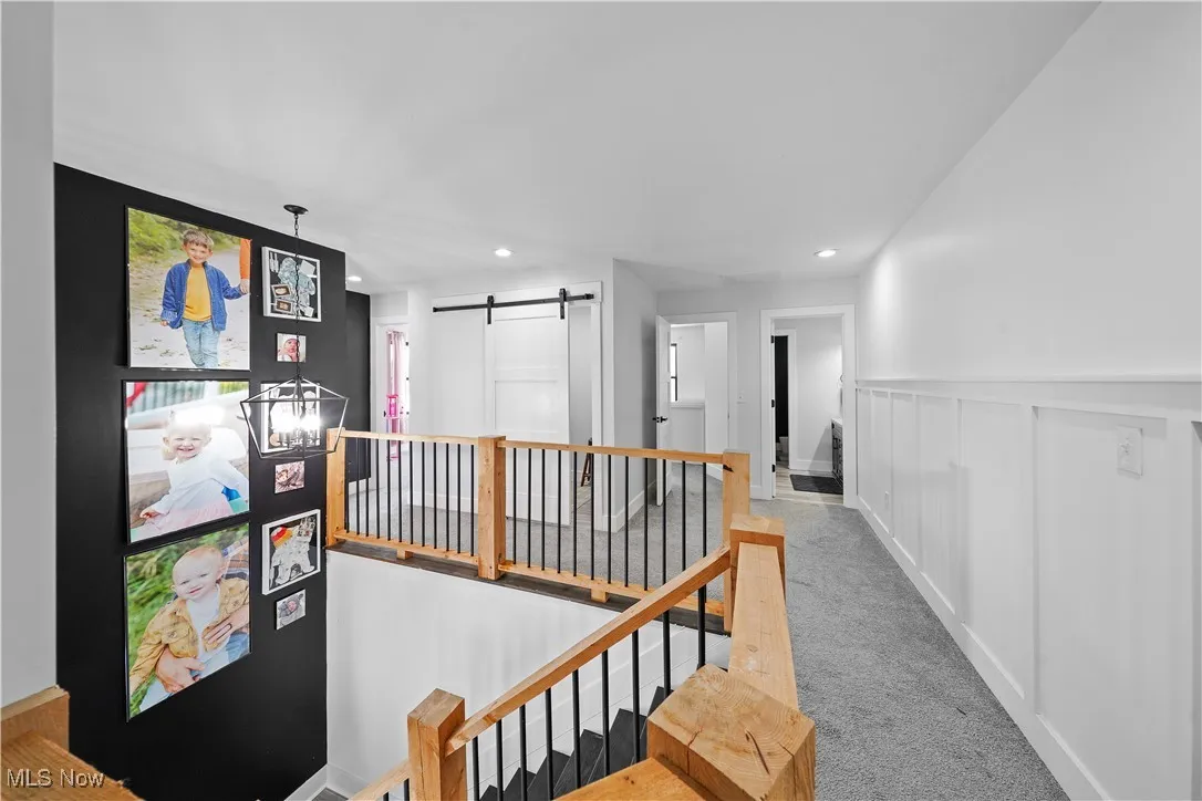 Hallway with a barn door, wainscoting, carpet, an upstairs landing, and recessed lighting