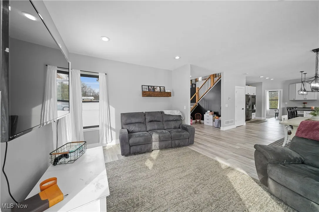 Living area with light wood-style floors, baseboards, visible vents, and stairs