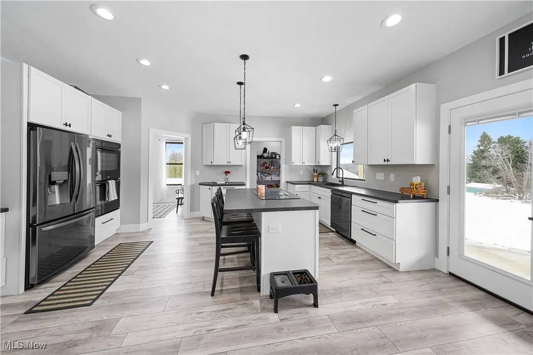 Kitchen featuring dark countertops, a center island, black appliances, light wood finished floors, and recessed lighting