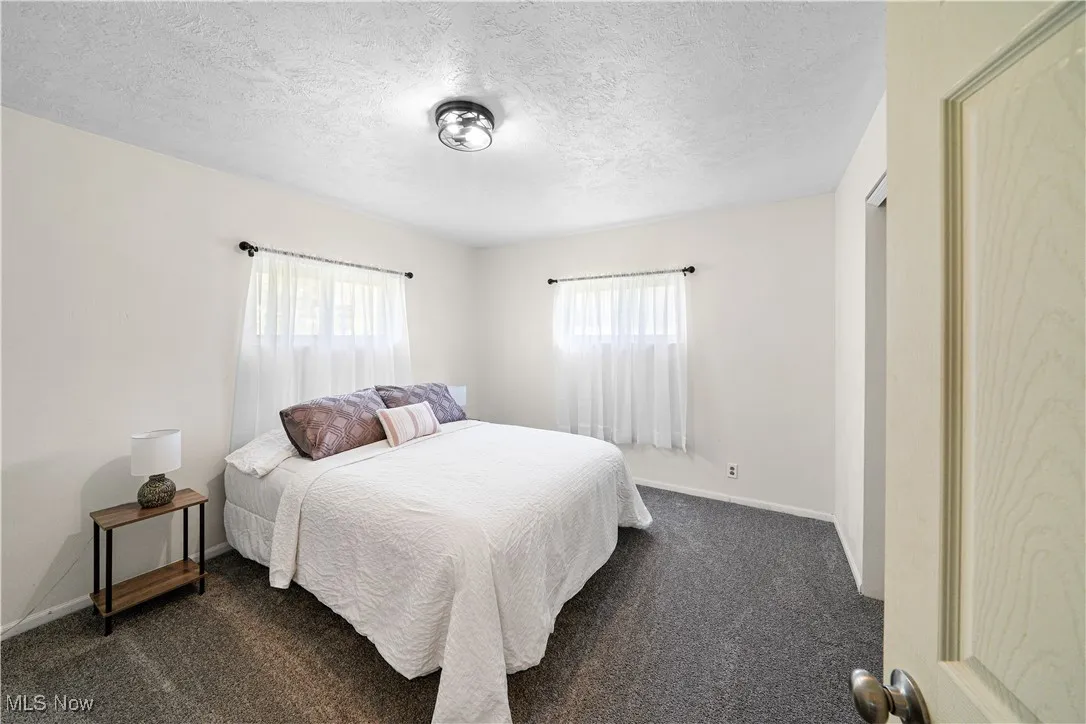 Bedroom featuring baseboards, dark colored carpet, multiple windows, and a textured ceiling