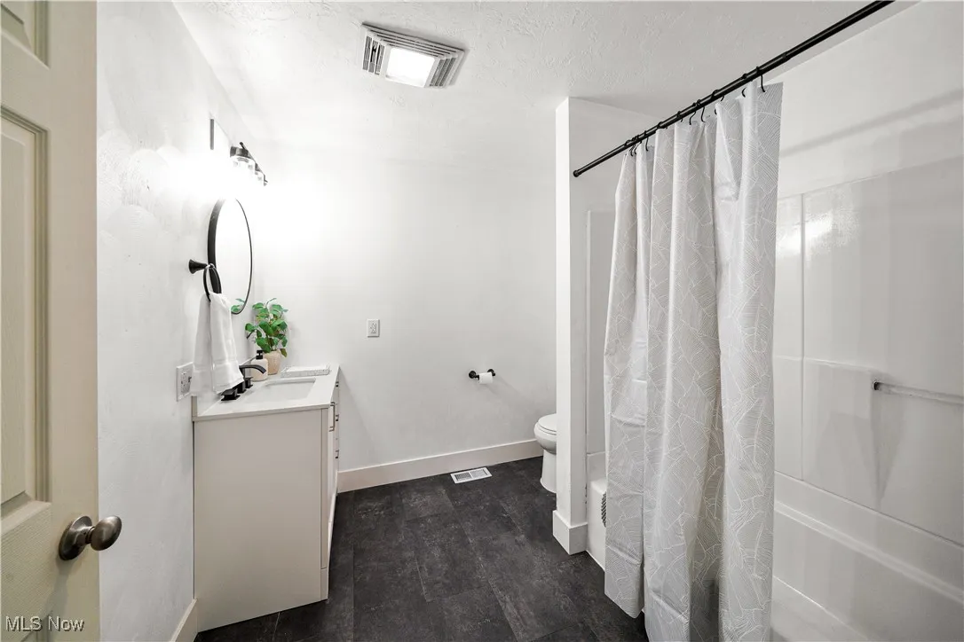 Full bathroom with visible vents, toilet, vanity, shower / bath combo with shower curtain, and baseboards
