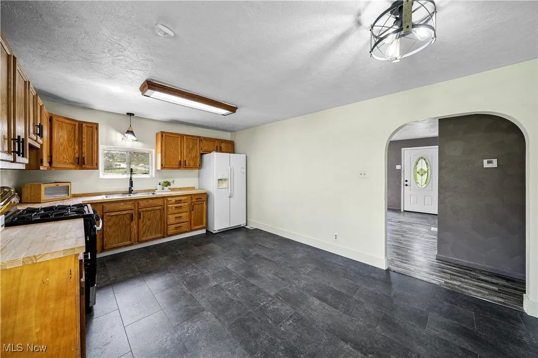 Kitchen featuring arched walkways, a sink, white fridge with ice dispenser, and black gas range oven