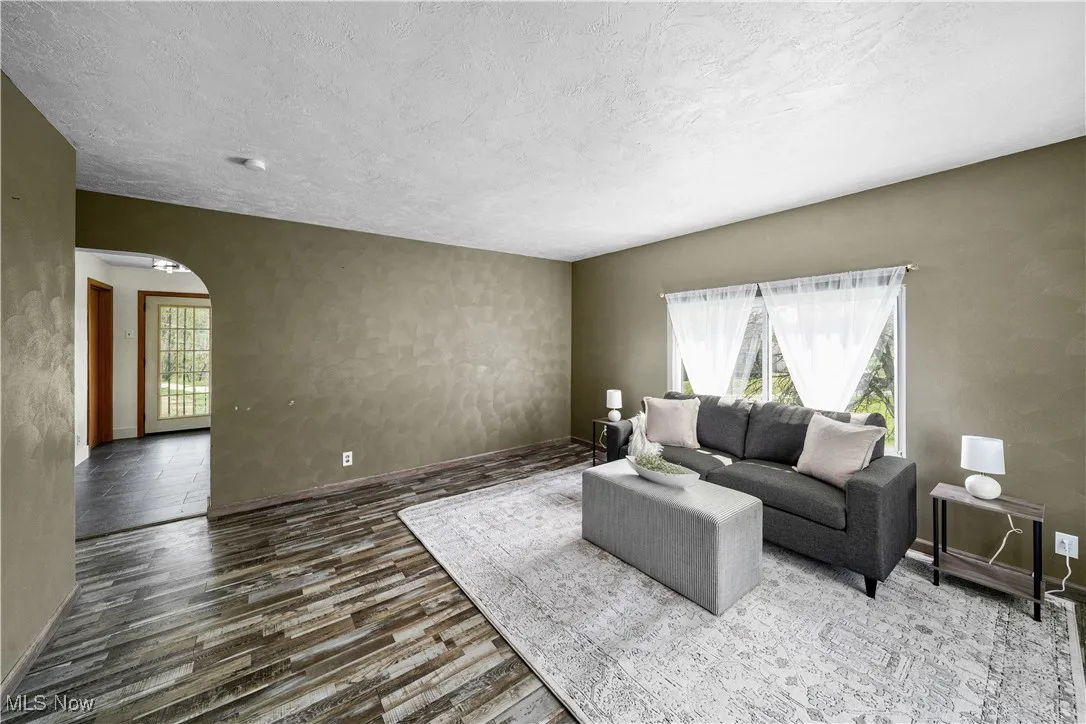 Living room featuring arched walkways, wood finished floors, a textured ceiling, and baseboards