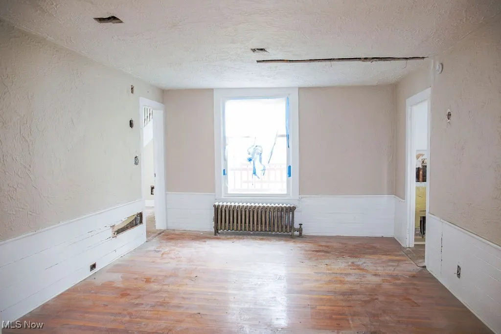 Unfurnished room with radiator heating unit, wood finished floors, a textured ceiling, and a wainscoted wall