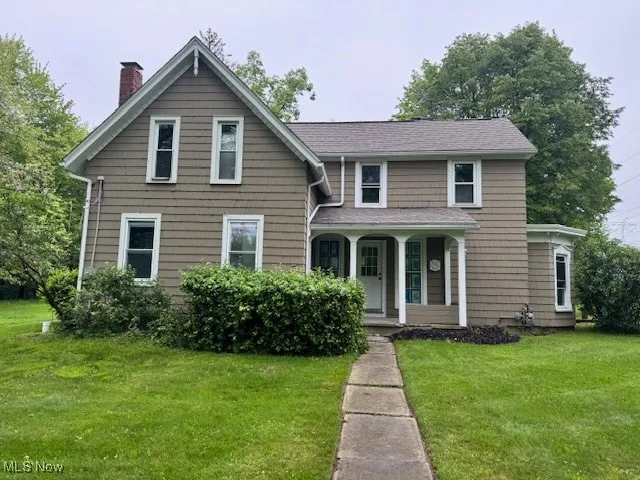 View of front of house with covered porch, a front yard, and a chimney