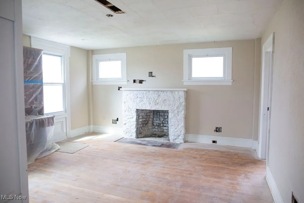 Unfurnished living room with a fireplace, wood finished floors, a healthy amount of sunlight, and baseboards