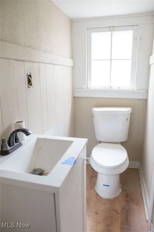 Half bathroom with a wainscoted wall, wood finished floors, vanity, and toilet