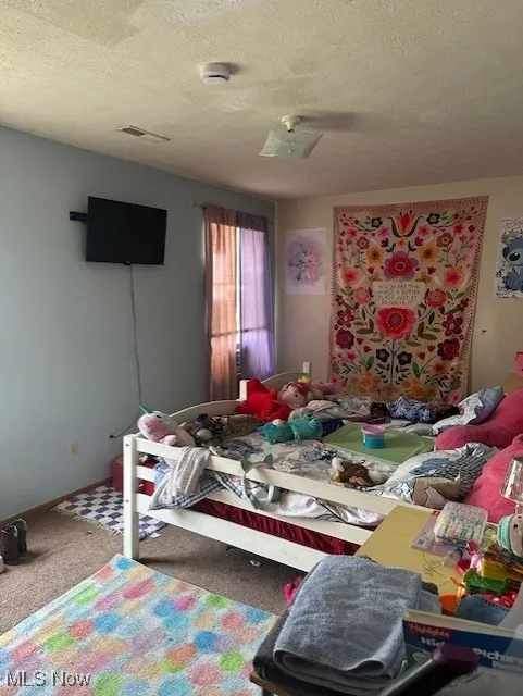 Bedroom with carpet, a textured ceiling, ceiling fan, and visible vents