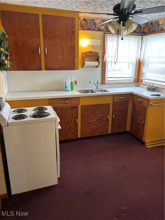 Kitchen with ceiling fan, range, light countertops, and a sink