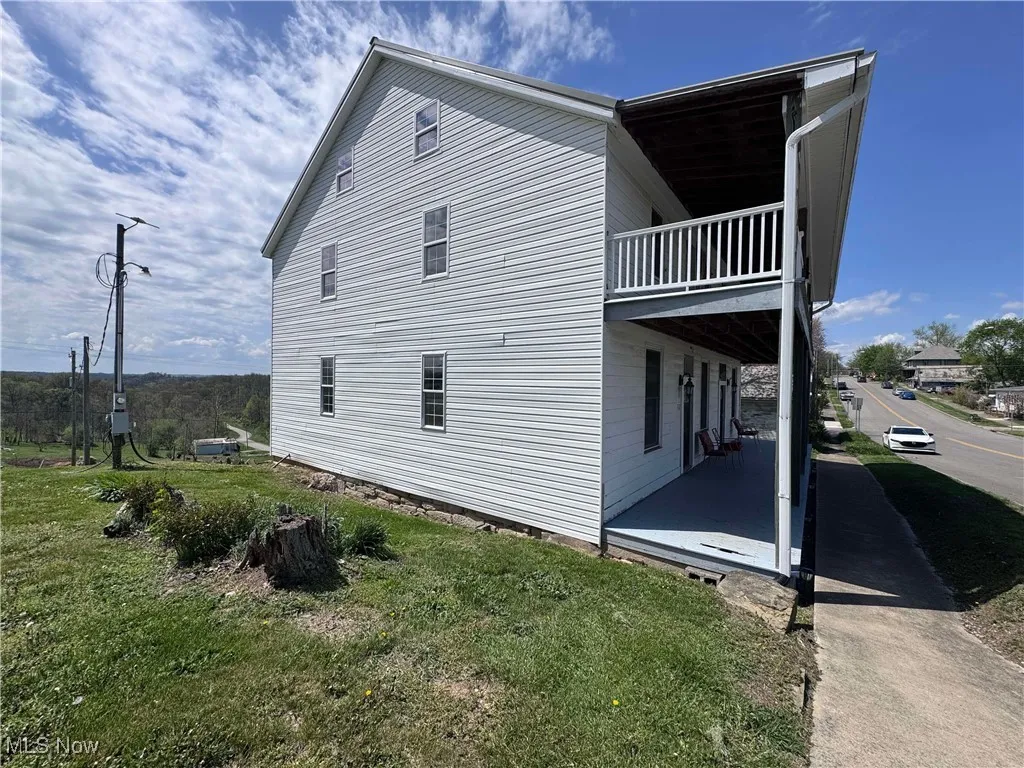 View of property exterior featuring a lawn, a balcony, and a patio