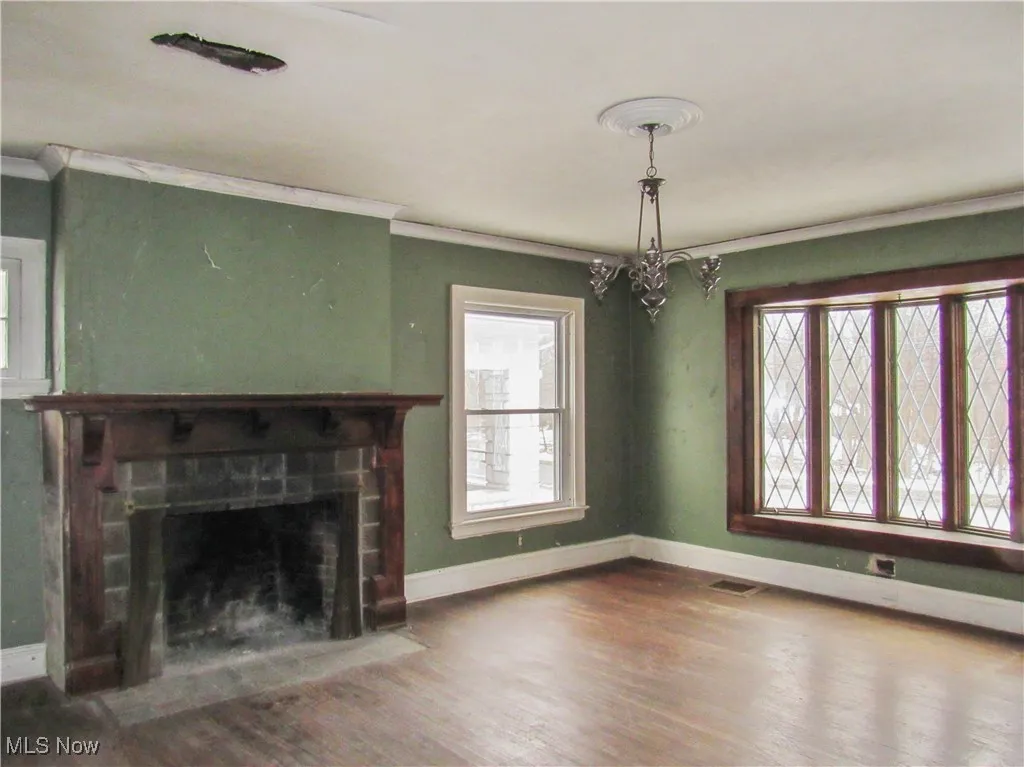 Unfurnished living room with baseboards, crown molding, a brick fireplace, and wood finished floors