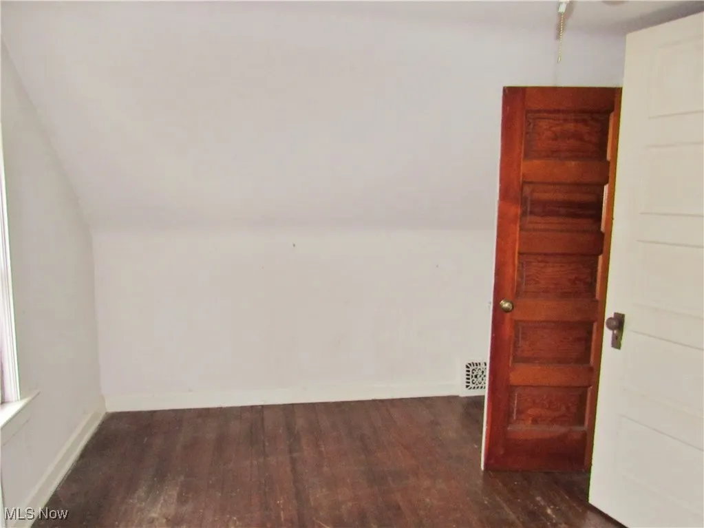 Spare room with dark wood finished floors, lofted ceiling, visible vents, and baseboards