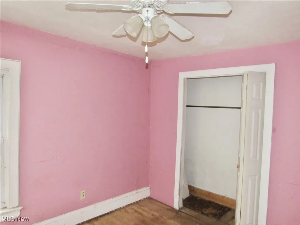 Unfurnished bedroom featuring wood finished floors, a closet, baseboards, and ceiling fan