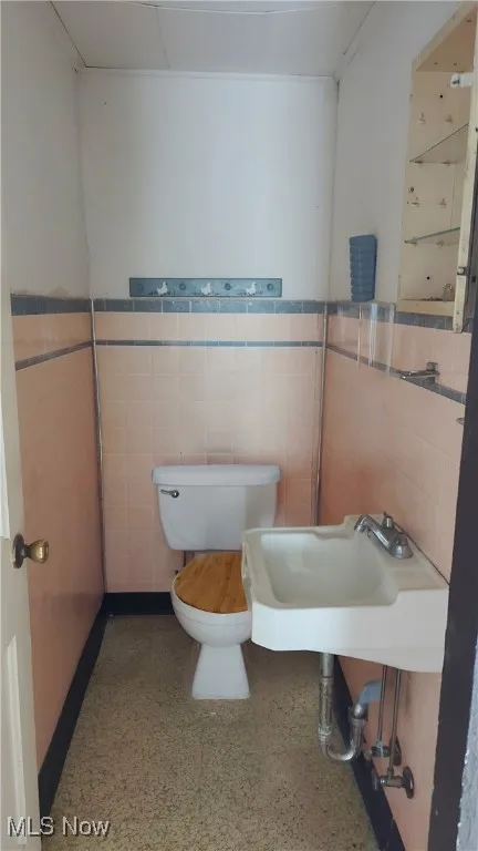 Bathroom with a sink, a wainscoted wall, toilet, and tile walls