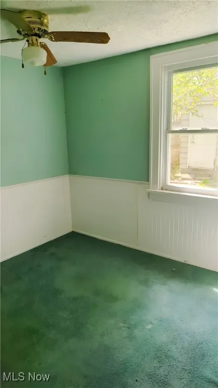 Empty room featuring ceiling fan, wainscoting, carpet flooring, and a textured ceiling