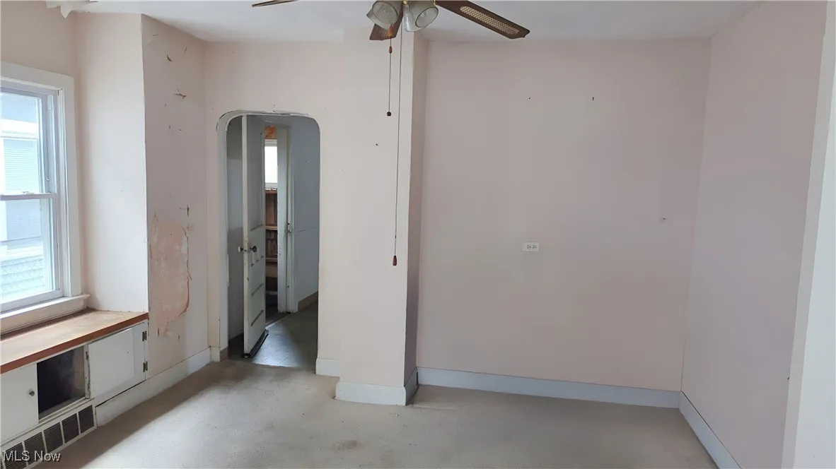 Unfurnished room with arched walkways, baseboards, a ceiling fan, and concrete floors