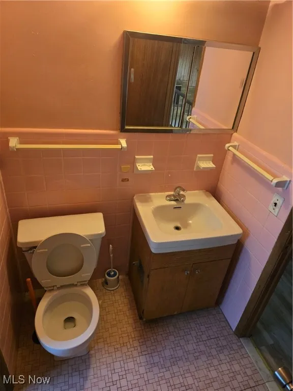 Bathroom featuring tile walls, toilet, vanity, and a wainscoted wall