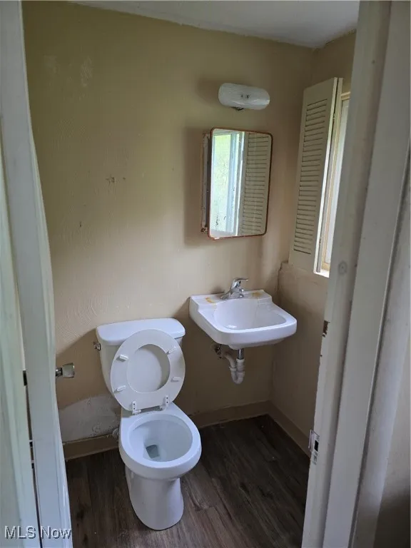Half bathroom in the basement featuring wood finished floors, toilet, a sink, and baseboards