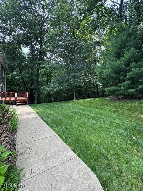 View of grassy yard with a deck and a wooded view