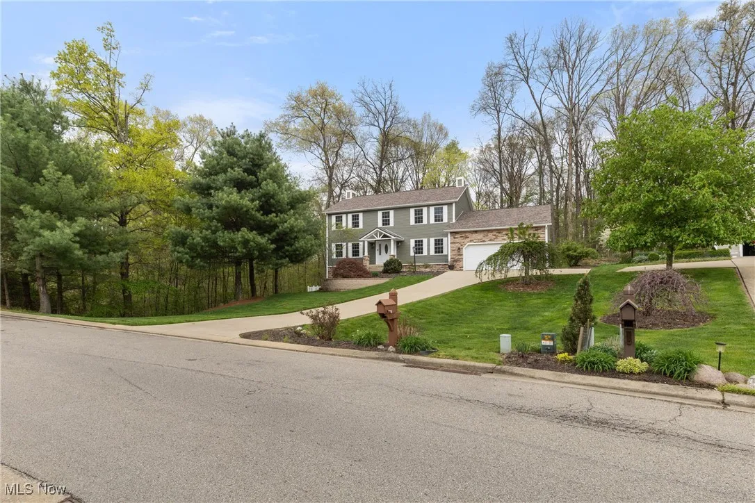 View of front facade featuring a front lawn, driveway, stone siding, and a garage